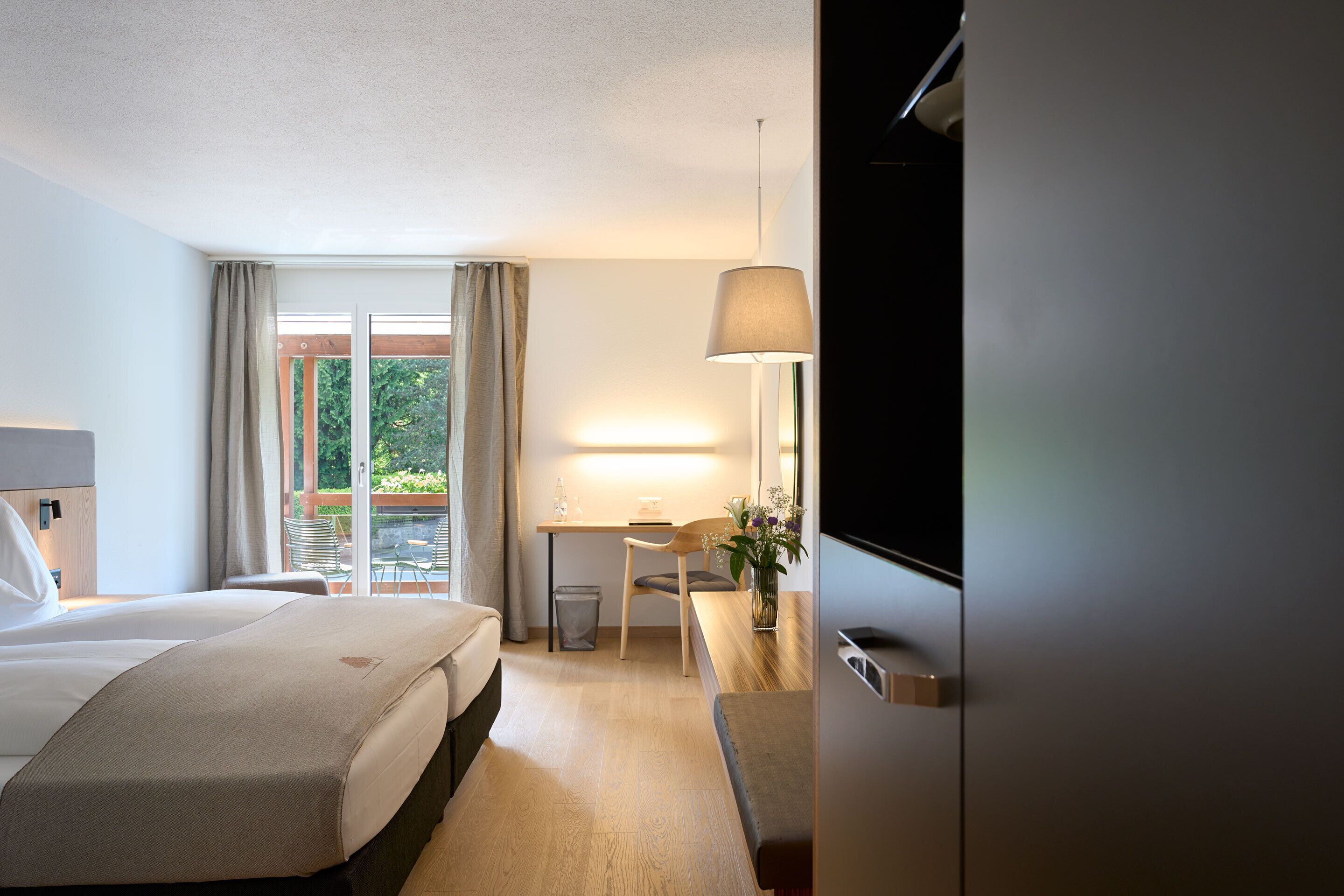 Habitación de hotel con cama, escritorio, silla, televisor y vistas al exterior.