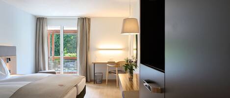 Habitación de hotel con cama, escritorio, silla, televisor y vistas al exterior.