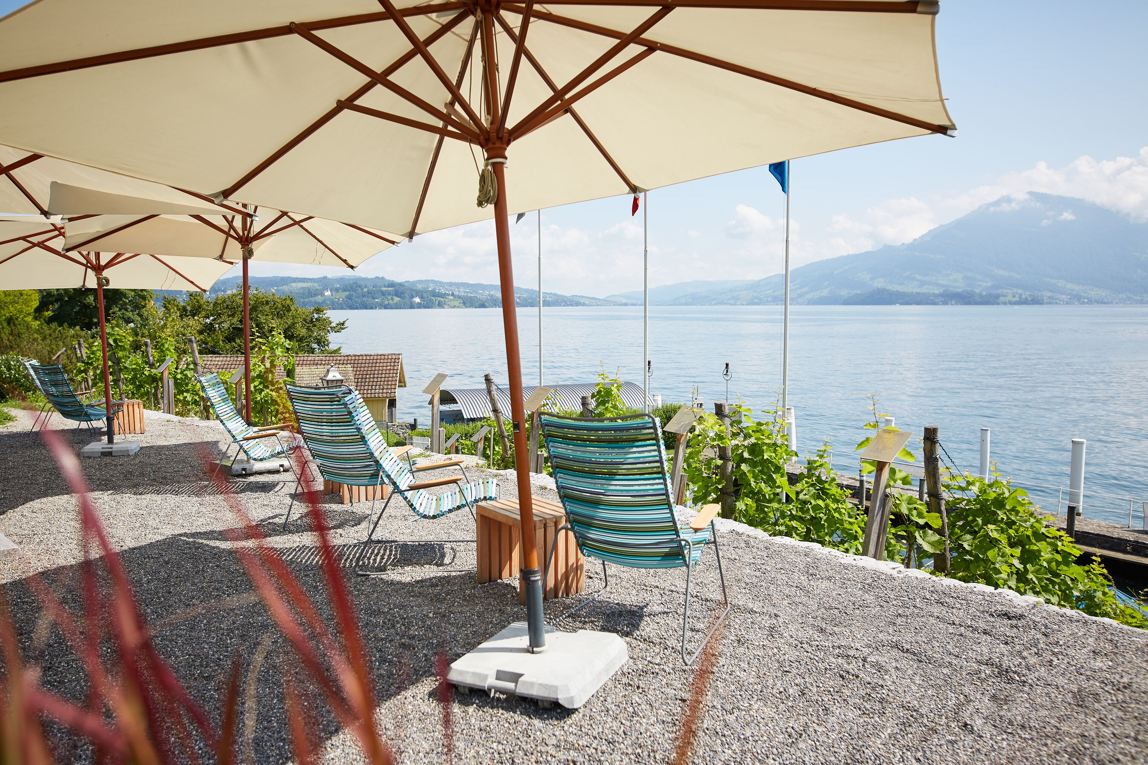 Une terrasse avec des sièges extérieurs, comprenant des chaises et des tables, donnant sur une étendue d’eau avec des montagnes en arrière-plan.
