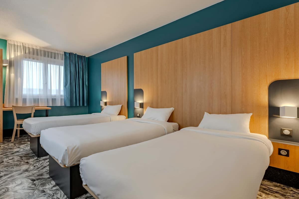 Una habitación de hotel con tres camas, un escritorio y una silla.