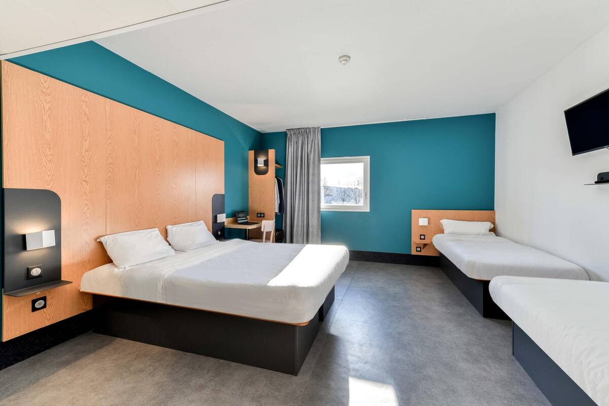 Una habitación de hotel con una cama grande, otra más pequeña, un escritorio, una silla, un televisor y una ventana.