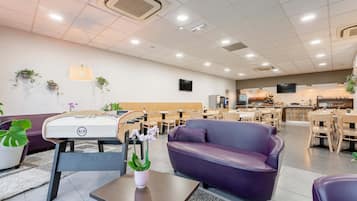Een moderne hotellobby met een paarse bank, een houten tafel met een bloevas, en een zithoek met stoelen en tafels.