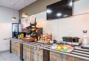 A breakfast bar with a variety of food items, a coffee station, and a TV mounted on the wall.