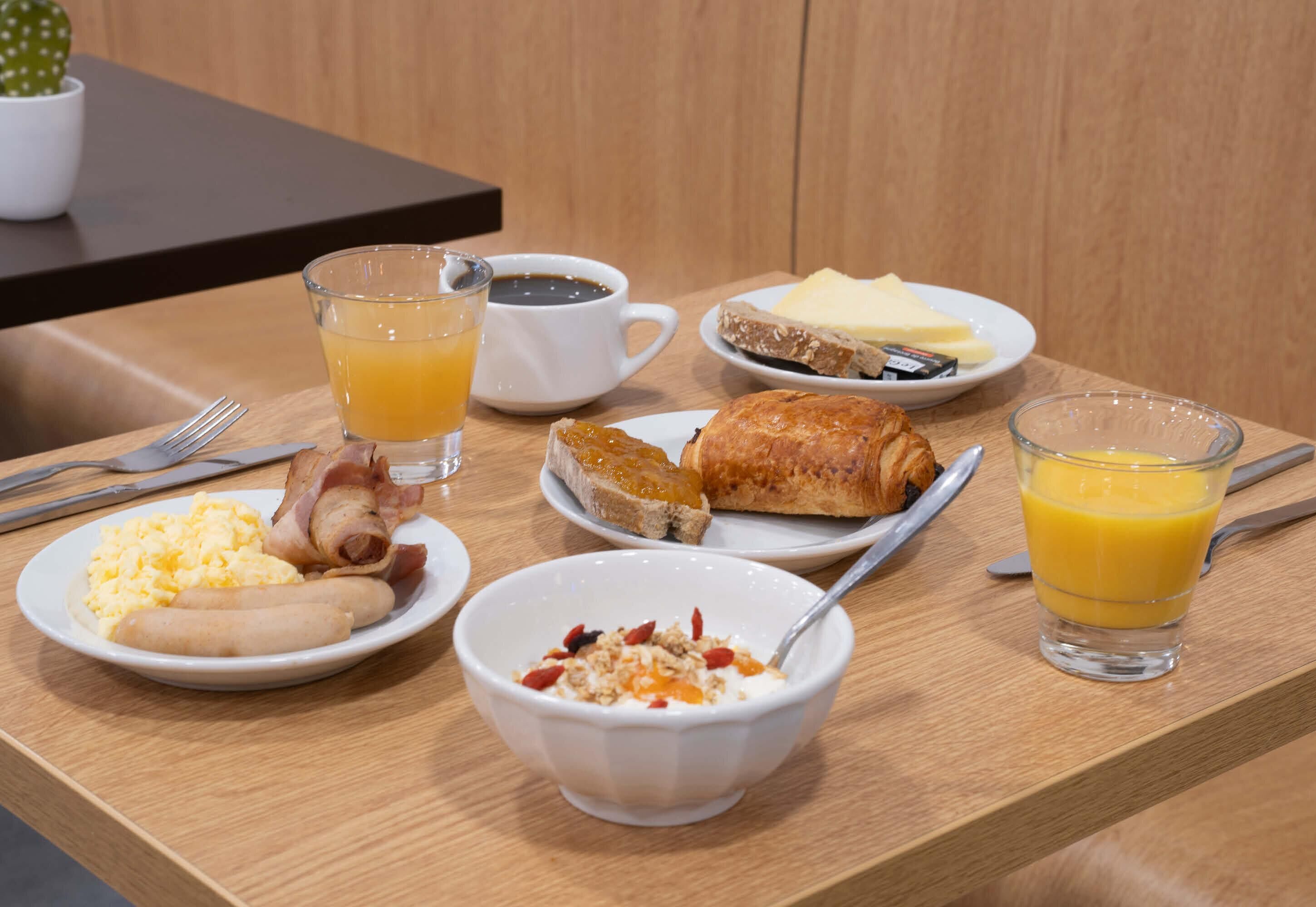 A breakfast table with plates of eggs, sausage, toast, and a croissant, accompanied by glasses of orange juice and coffee.