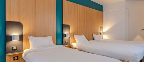 A hotel room with two beds, wooden headboards, wall-mounted lights, and a door.