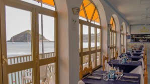 A restaurant with tables set for dining, large windows with a view of the sea, and a bar area with shelves of bottles. - Hotel Regina del Mare (Barano d'Ischia)