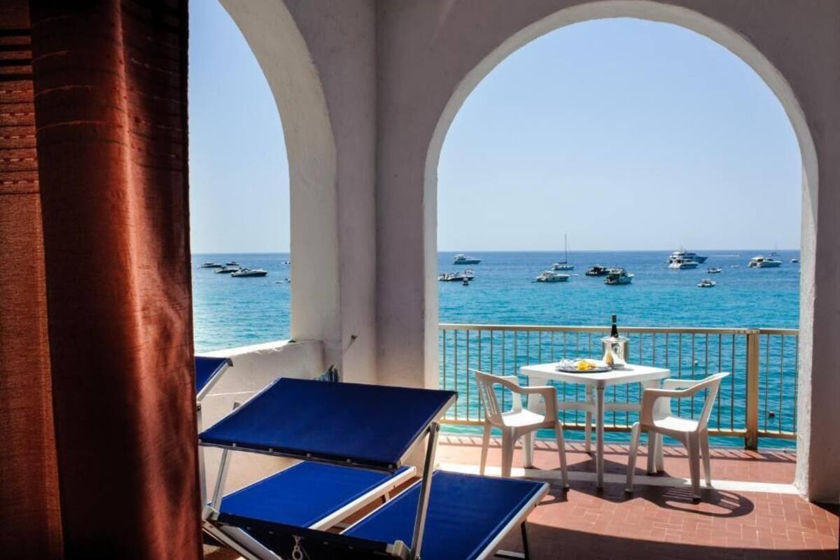 Un balcon avec vue sur la mer, comprenant une table et des chaises, ainsi que deux fauteuils bleus.