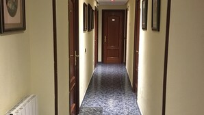 A hallway with a marble floor, wooden doors, and framed pictures on the walls. - Hostal Conchita Legazpi (Madrid)