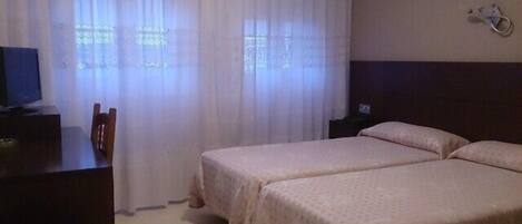 A hotel room with two beds, a desk with a chair, a TV, and a window with curtains.