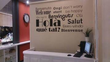 Una recepción con un panel que muestra mensajes de bienvenida en varios idiomas y un reloj.
