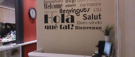 A reception desk with a wall featuring multilingual welcome messages and a clock.