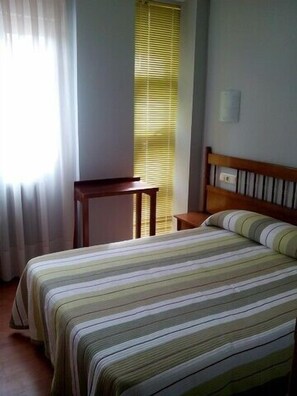 A bedroom with a bed, a bedside table, and a window with blinds. - Hotel Muradana (Muros)