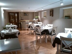 A dining area with round tables and white chairs, a bar area, and a wooden floor. - Hotel Muradana (Muros)
