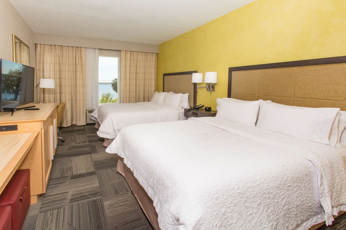 Habitación de hotel con dos camas, un escritorio y televisión, y vistas al exterior.
