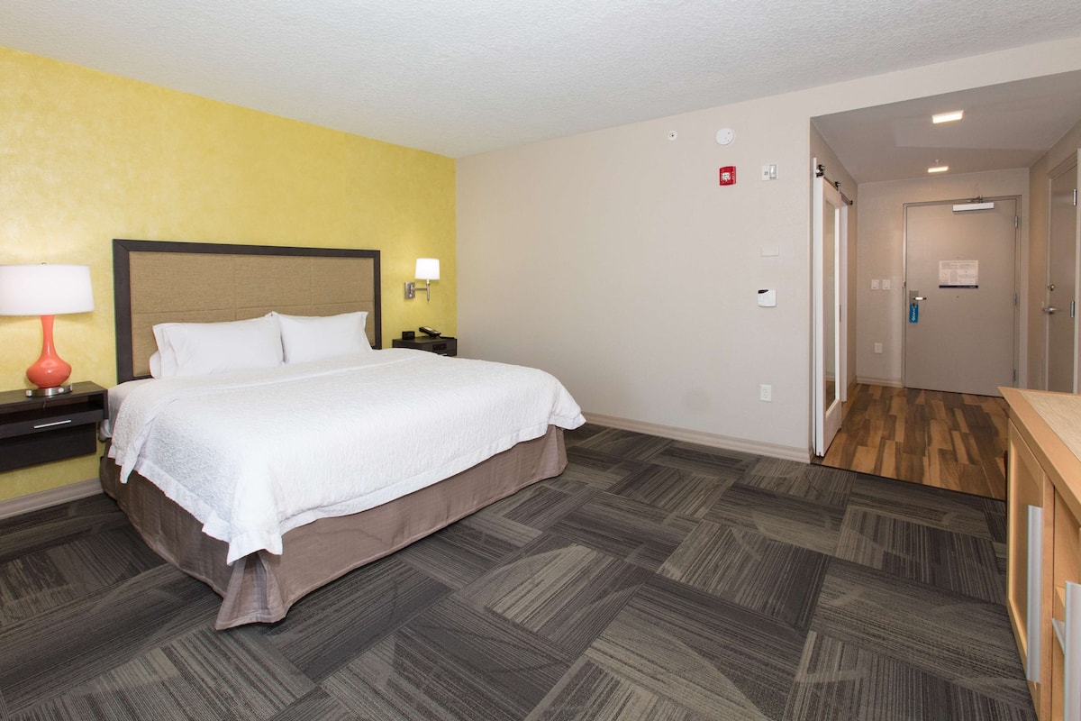 Una habitación de hotel con una cama, mesitas de noche, una lámpara y suelo de madera.