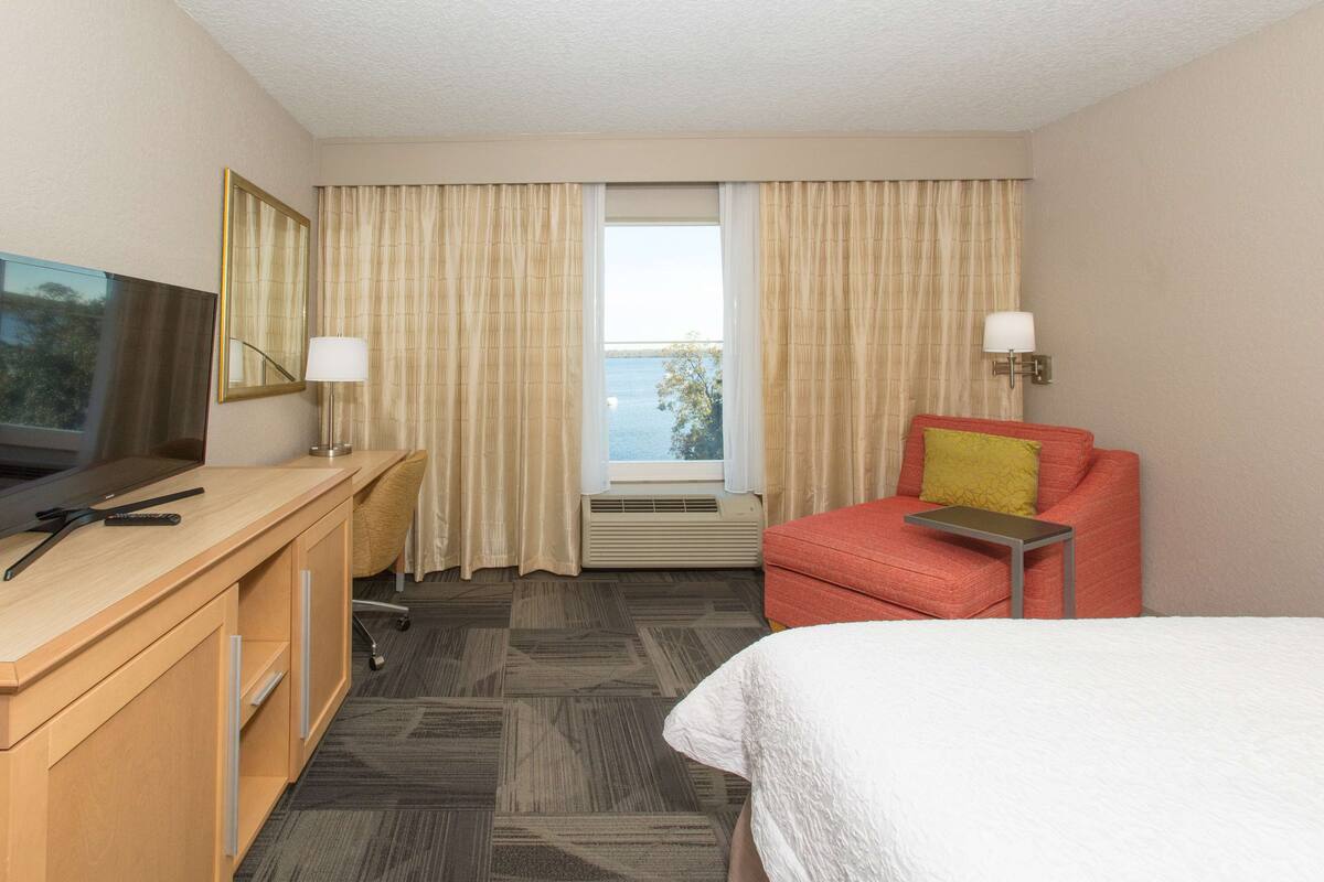Una habitación de hotel con una cama, un escritorio con televisor, una silla y una ventana con cortinas.