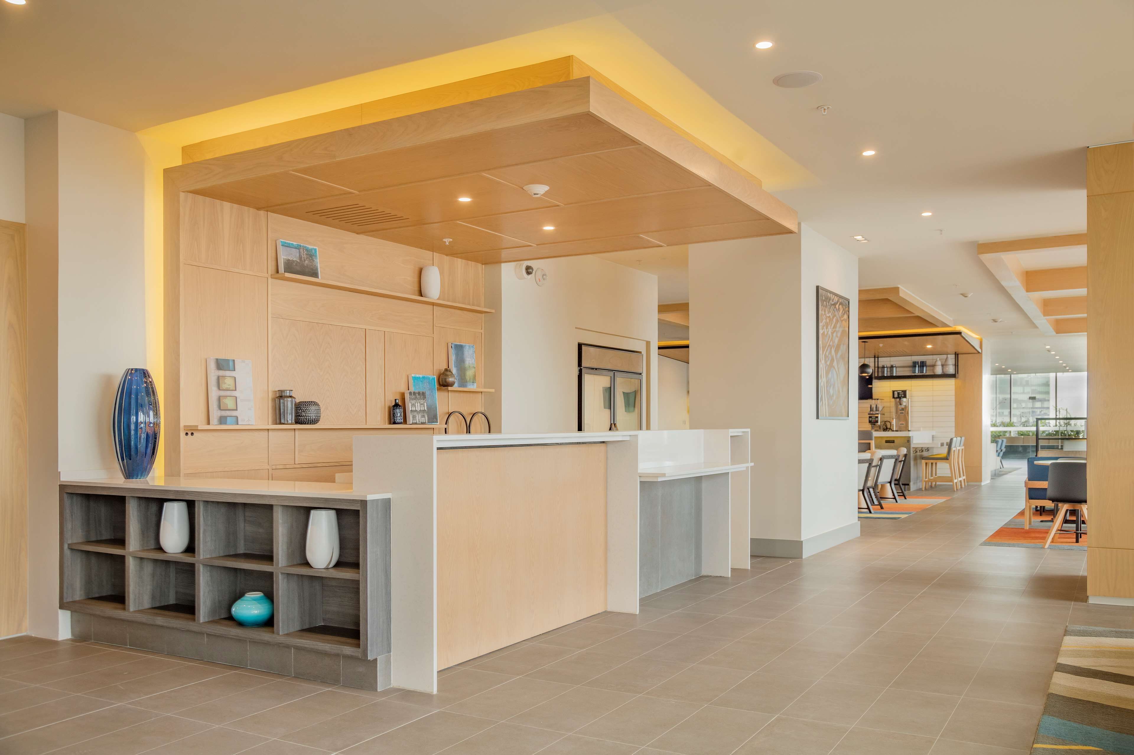 A modern reception area with a wooden reception desk, shelves with decorative items, and a view into the adjacent dining area.