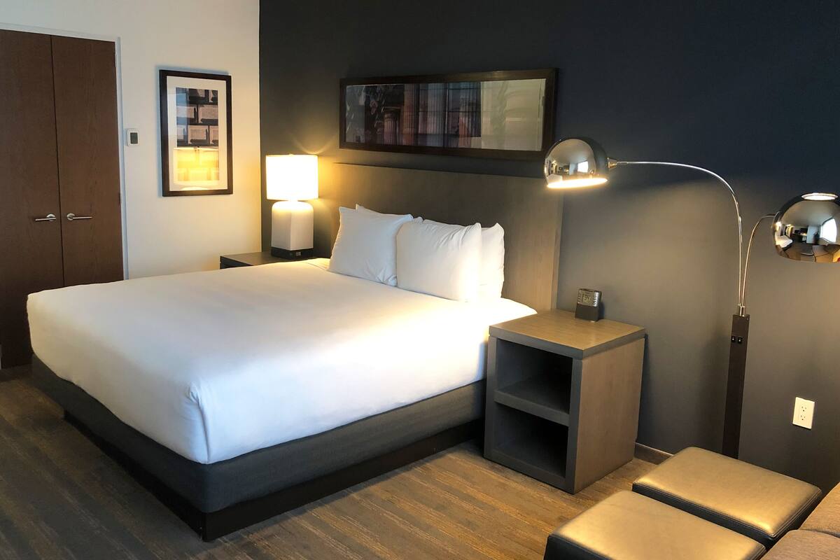 A hotel room with a large bed, bedside tables, a nightstand, a lamp, a clock, and a wardrobe.