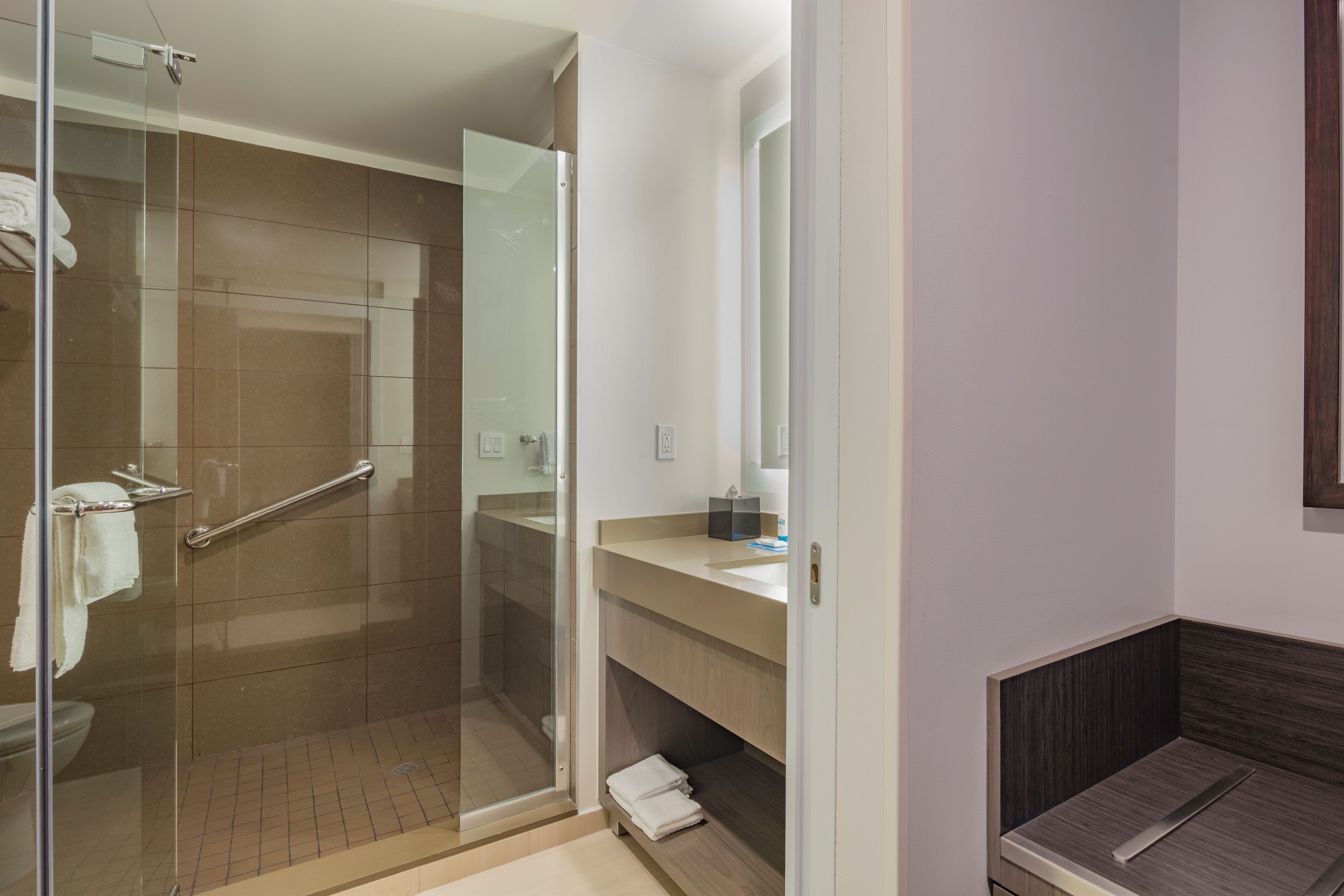 A modern bathroom with a glass shower enclosure, a vanity with a mirror, and a wooden bench.