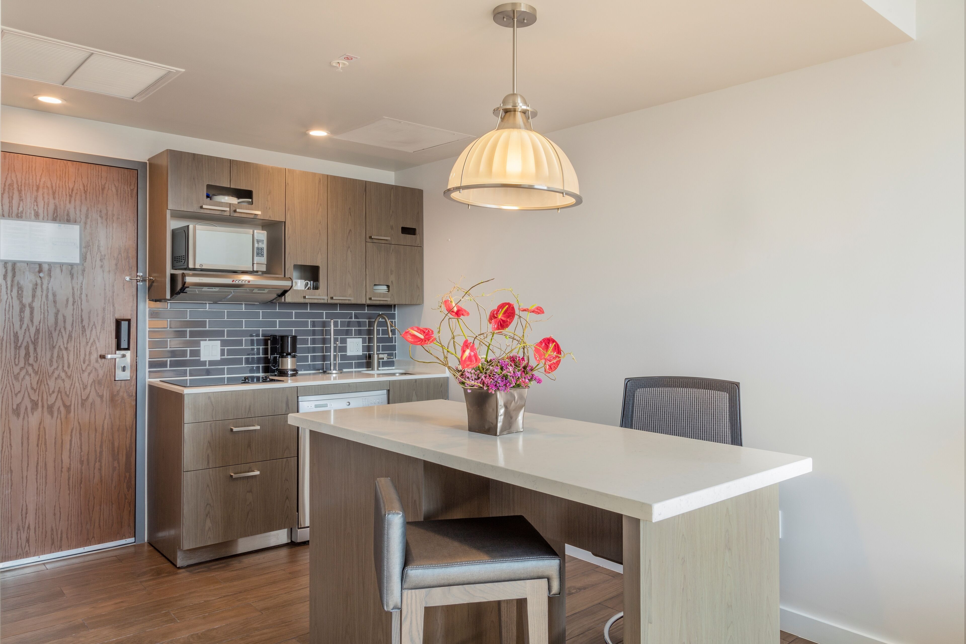 A modern kitchen with wooden cabinets, a white countertop, and a dining area with a chair.