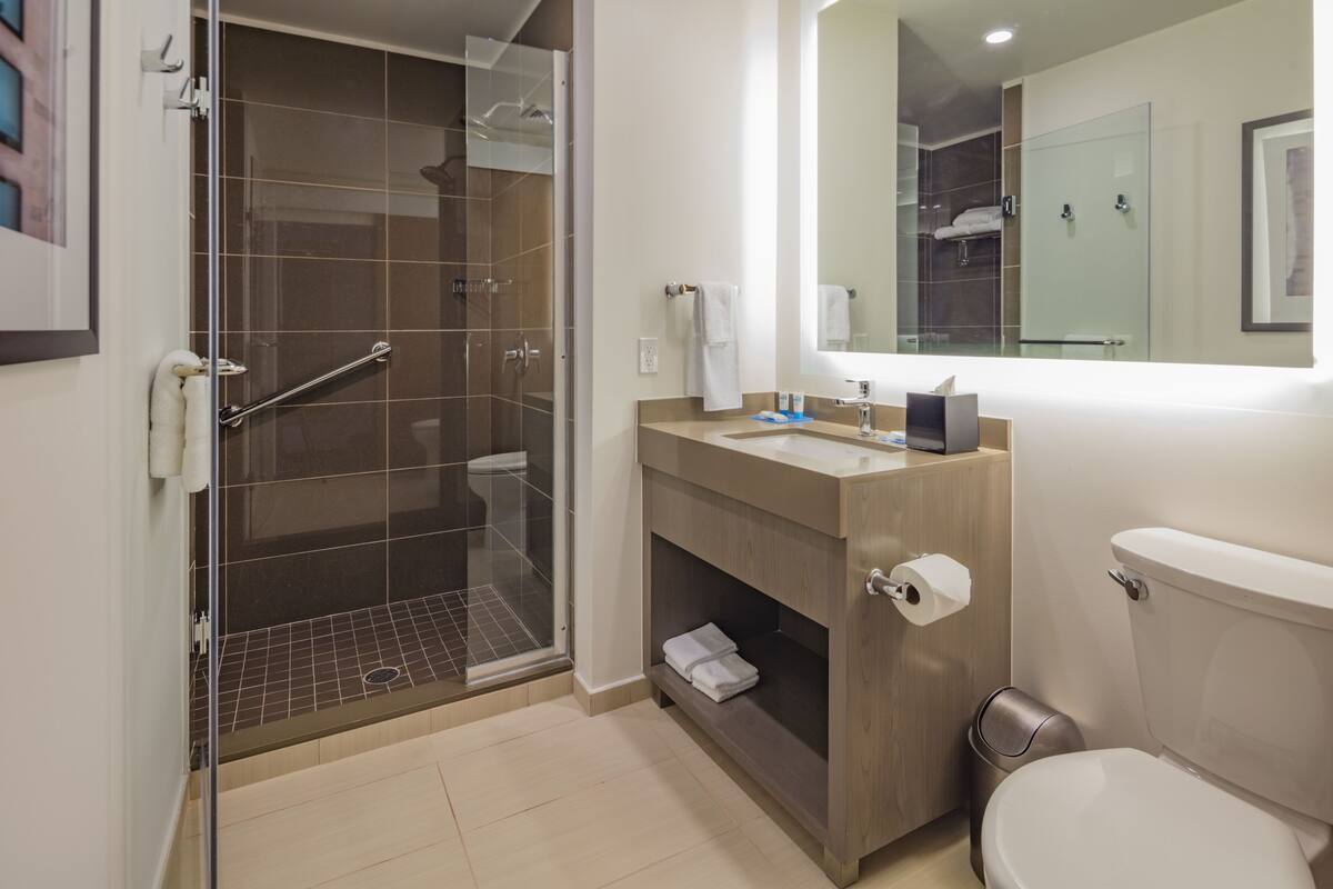 A modern bathroom with a glass-enclosed shower, a wooden vanity, a toilet, and a large mirror.