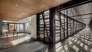 Un moderno vestíbulo de hotel con techo de madera, una recepción y un separador de vidrio con listones de metal.