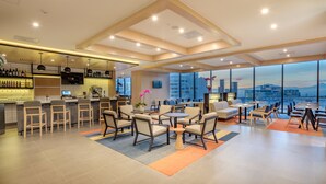 Un moderno vestíbulo de hotel con zona de bar, arreglos de asientos y grandes ventanales con vistas a la ciudad.