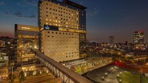 Un hotel moderno con varios pisos, fachada de vidrio y terraza en la azotea.