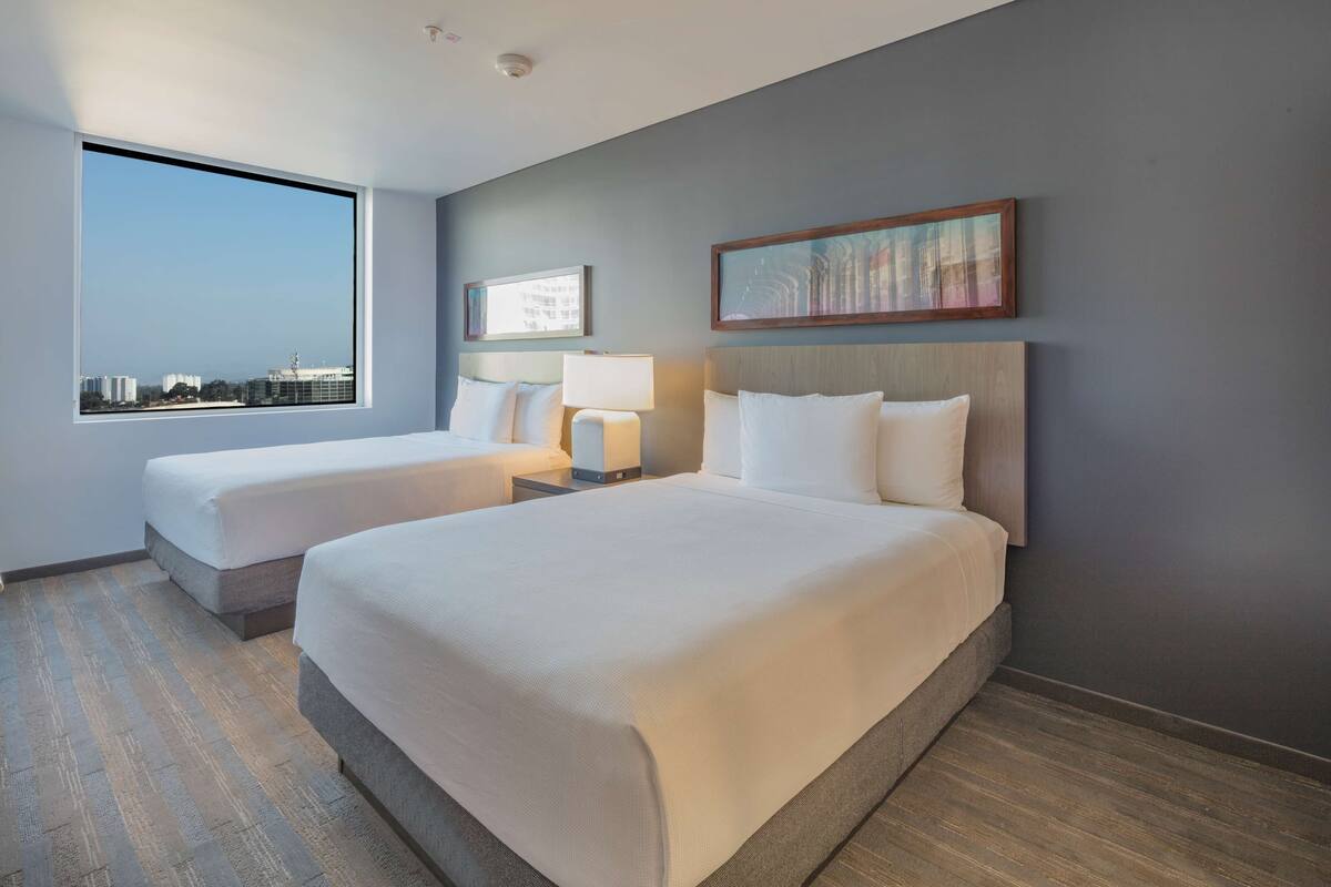 A hotel room with two beds, a large window, and a city view.