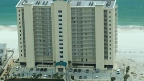 A high-rise hotel with multiple floors, a parking lot, and a beach view.