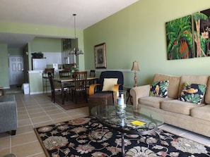 A living room with a glass coffee table, a sofa with patterned cushions, a dining area with a table and chairs, and a kitchen in the background. - Windemere by Tern Key Realty (Pensacola)