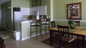 A compact kitchen with white cabinets, a microwave, and a sink. There is a dining area with a wooden table and chairs.