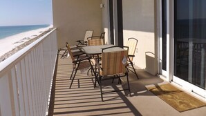 A balcony with a table and chairs, overlooking a beach.