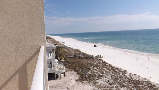A beach view from a balcony with a sandy beach, ocean, and a building with a staircase leading down to the beach.