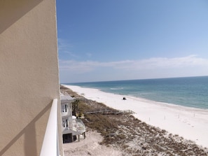 A beach view from a balcony with a sandy beach, ocean, and a building with a staircase leading down to the beach. - Windemere by Tern Key Realty (Pensacola)