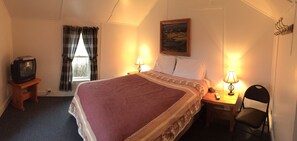 A hotel room with a bed, two bedside tables with lamps, a chair, a television on a stand, a window with curtains, and a painting on the wall. - Whistling Swan Motel (East Glacier Park)