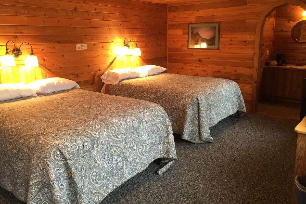 A cabin with two beds, a wooden ceiling, a framed picture, and a small kitchen area.