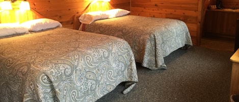 Eine Hütte mit zwei Betten, Holzboden, einem gerahmten Bild und einer kleinen Küchenzeile.