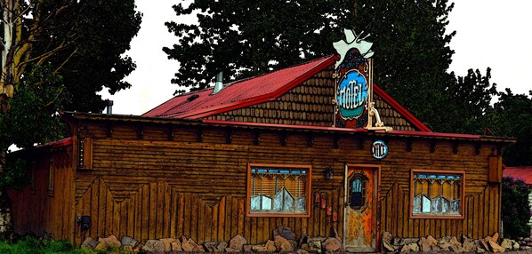 A rustic wooden building with a red roof, a sign indicating it is a hotel, and a bell tower. - Whistling Swan Motel (East Glacier Park)