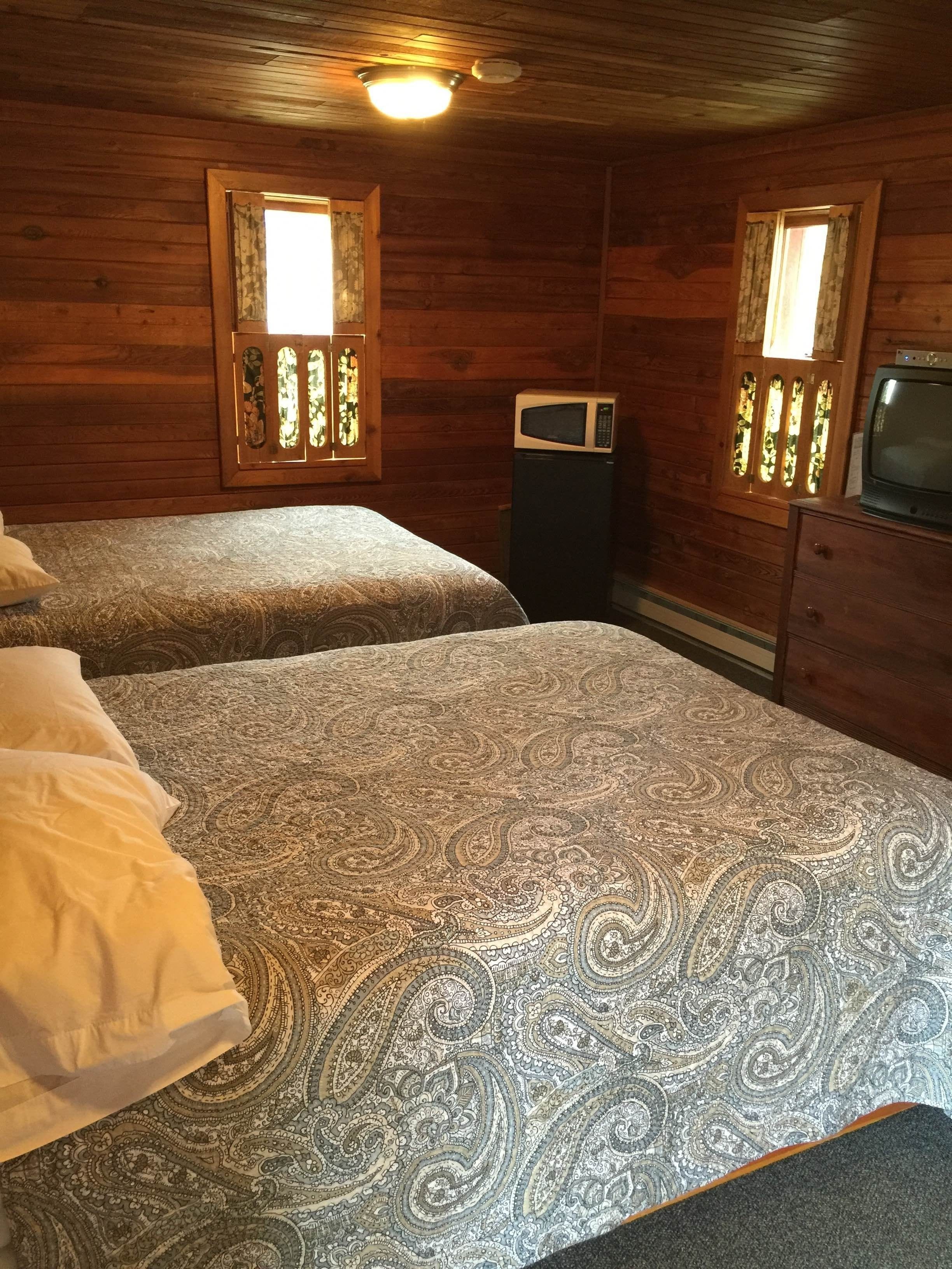 A room with two beds, wooden walls, a microwave, and a television.