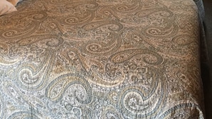 Una habitació acollidora amb parets de fusta, dos llits amb roba de llit estampada, un quadre a la paret i una finestra amb cortines.
