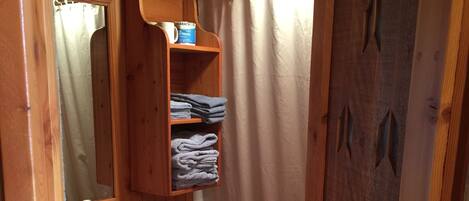 Een houten badkamer met een houten wastafel, een wastafel, een spiegel, een handdoekhouder en een douchegordijn.
