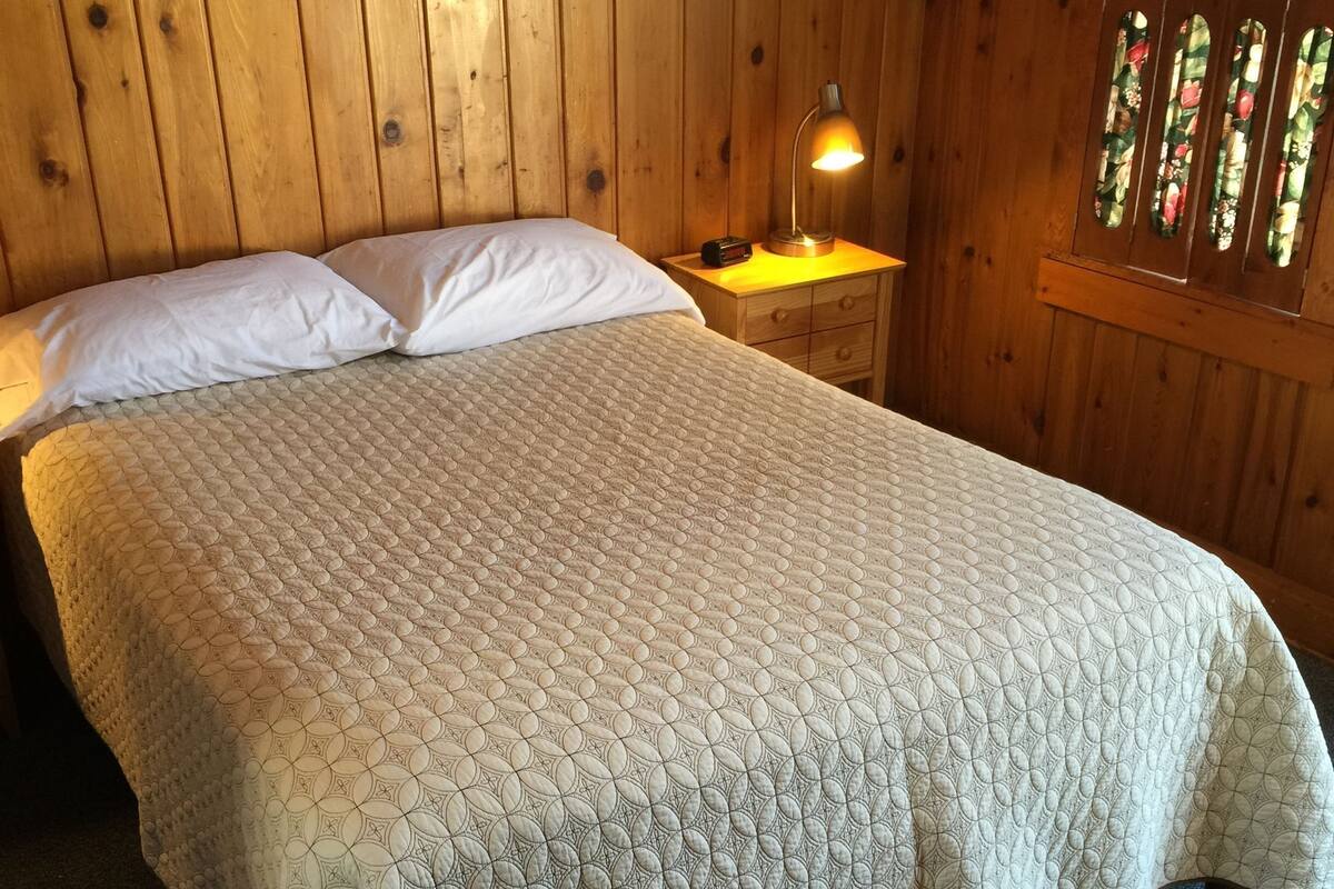A bed with a quilted cover, a bedside lamp, and a wooden headboard.