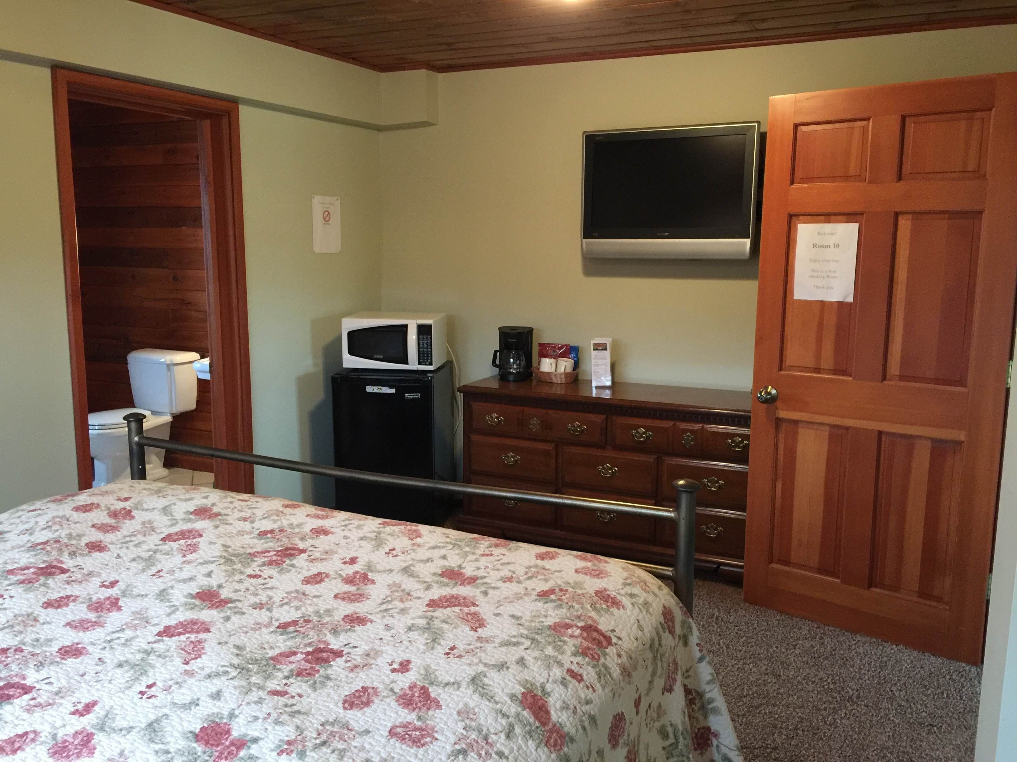 A bedroom with a bed, a dresser, a microwave, a television, and a door labeled "Room 10".