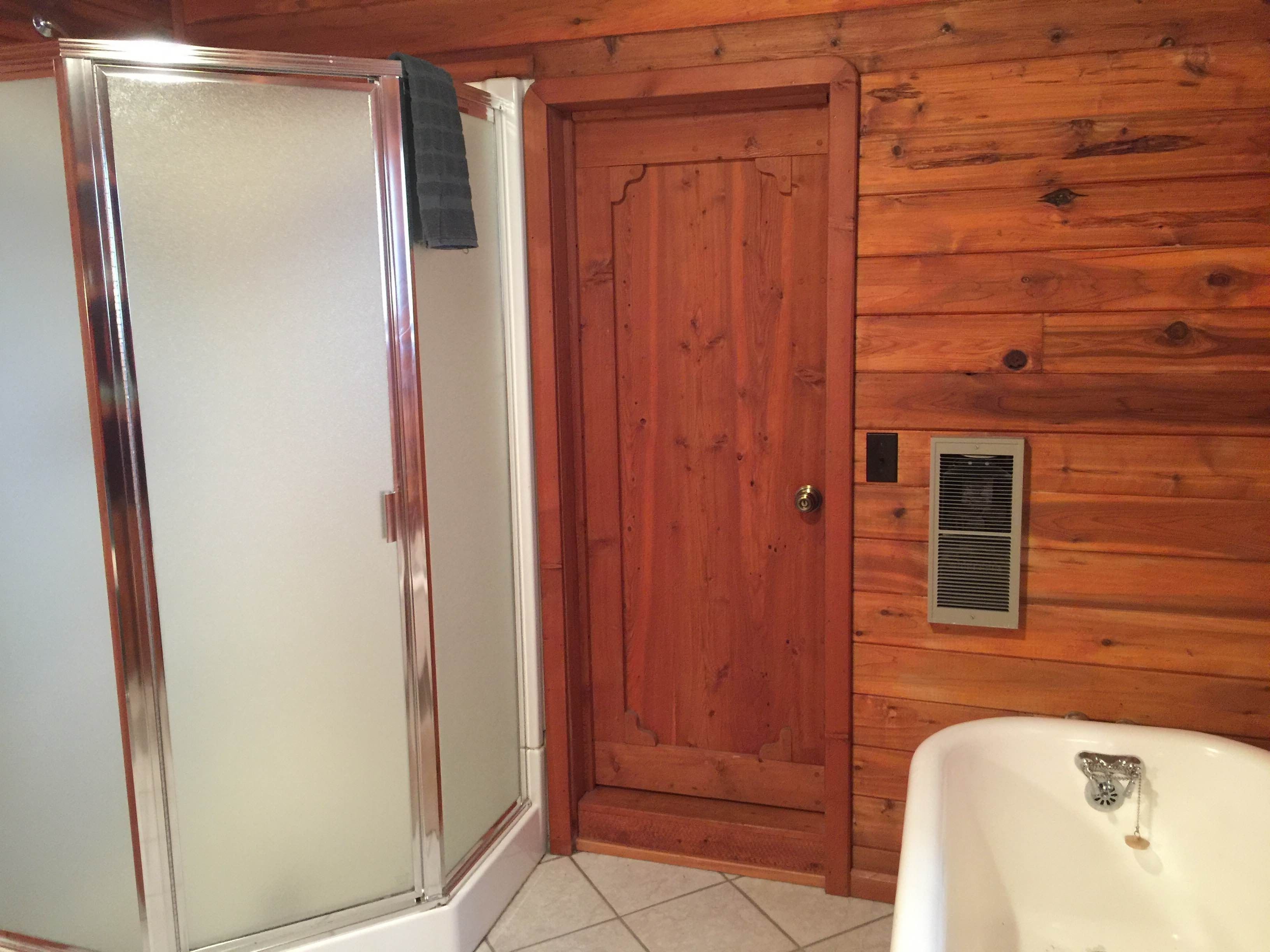 A bathroom with a glass shower enclosure, a wooden door, and a white sink.