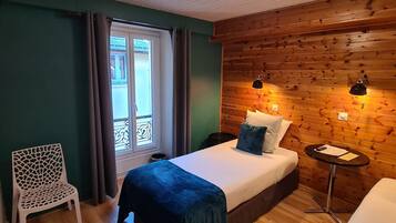 A room with a bed, a chair, a small table, and a wooden wall.