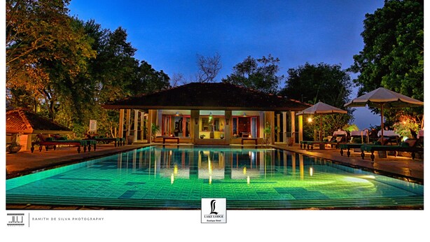 A poolside area with lounge chairs and umbrellas, a building with a tiled roof, and a clear sky.