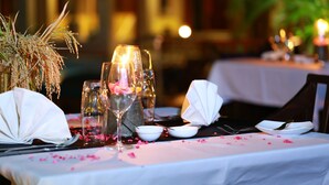 A table set for dining with a white tablecloth, clear glassware, and a vase with dried plants.