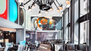A modern lounge area with leather seating, a large mural, and a ceiling with multiple light fixtures. - Motel One Basel (Basel)