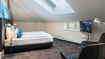 Une chambre d’hôtel moderne avec une lucarne, un lit recouvert de draps blancs, un téléviseur à écran plat, une chaise et une lampe de bureau.